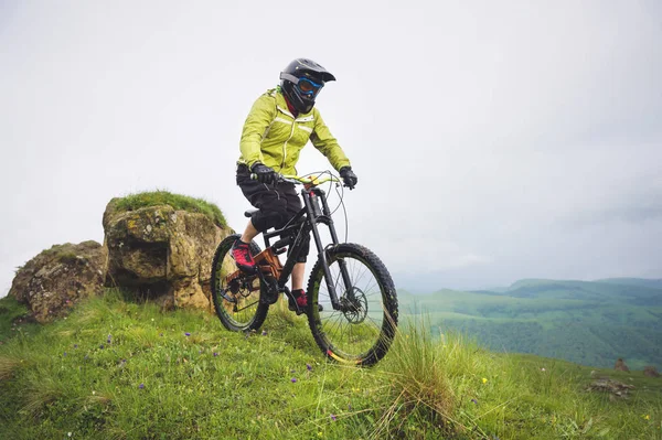 Hombre atleta envejecido en casco y máscara paseos por una ladera cubierta de hierba en una bicicleta de montaña. concepto de bicicleta de montaña cuesta abajo —  Fotos de Stock