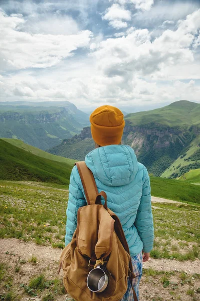 A kilátás a hátán egy turista lány egy hátizsák áll, és nézi a hegyi zöld völgyek és fennsík egy napsütéses napon az ég és a felhők. Utazási és idegenforgalmi koncepció — Stock Fotó