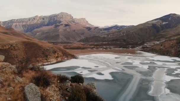 Вид з повітря на гірський схил і скеля на берег замерзлого гірського озера на тлі епічних скель і гір після заходу сонця в сутінках взимку. Низький ключ — стокове відео
