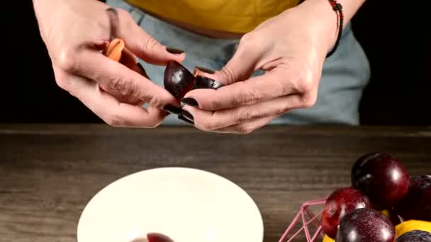 Close-up de mãos femininas em uma cozinha doméstica estão cortando bagas frescas com uma faca de ameixa e tirando um osso deles ao lado de um cesto de limões. O conceito de alimentos saudáveis e vitaminas — Vídeo de Stock
