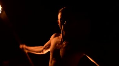 Close. Düşük anahtar. Uzun saçlı ve çıplak gövde ile genç erkek siyah bir gece video yavaş hareket açık havada yanan meşale döner. Modern fakir bir yanan personel ile hileler yapar