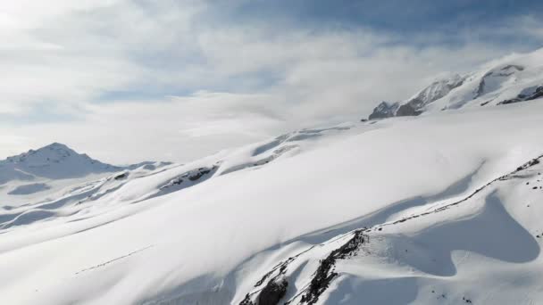 Vista aérea de un paisaje montañoso invernal. Las laderas rocosas cubiertas de nieve de la estación de la región sur de Elbrus con pistas de esquí en la nieve. Concepto de deportes de invierno — Vídeos de Stock