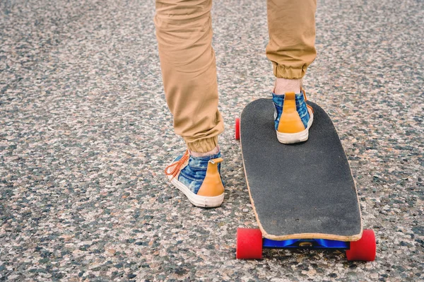 Close-up de pernas masculinas em rag sneakers em um longboard no fundo de asfalto ao pôr do sol. Grande skate com pernas de homem. Conceito de lazer juvenil — Fotografia de Stock