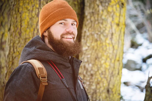 Крупним планом портрет усміхненого бородатого молодого чоловіка в капелюсі і рюкзак в хвойному лісі — стокове фото