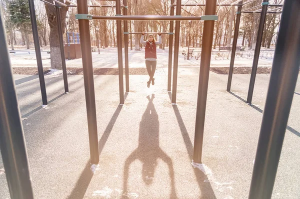 Attractive girl involved in sports workout on a horizontal bar on a sunny winter day. The concept of sports activities all year round — Stock Photo, Image