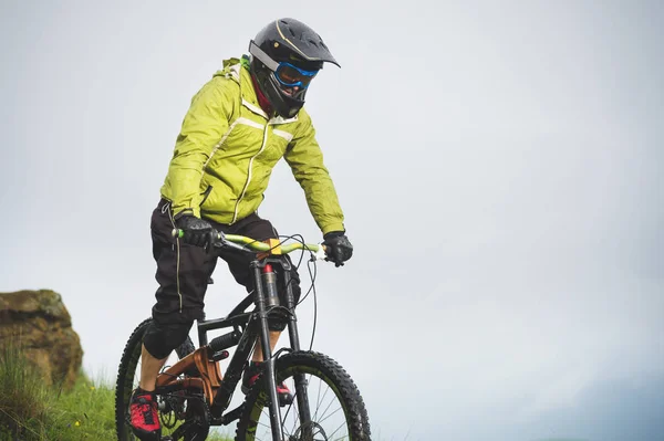 Atleta masculino envelhecido em capacete e máscara desce uma encosta gramada em uma bicicleta de montanha. Downhill conceito de bicicleta de montanha — Fotografia de Stock