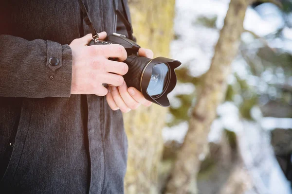 Close-up professional digital mirror camera in male hands in the winter forest. Photo travel concept