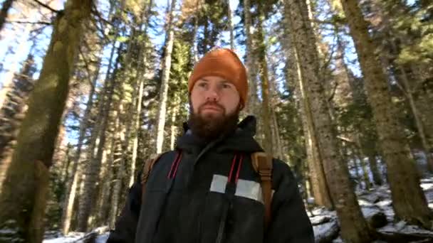 Porträtt av en skäggiga ung man med ryggsäck stående i en barrskog vinterskogen — Stockvideo