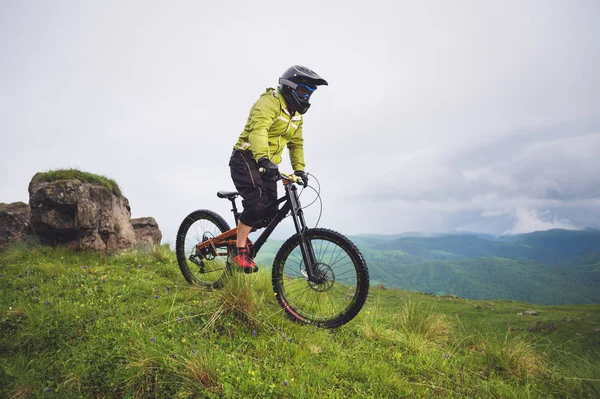 Hombre atleta envejecido en casco y máscara paseos por una ladera cubierta de hierba en una bicicleta de montaña. concepto de bicicleta de montaña cuesta abajo —  Fotos de Stock