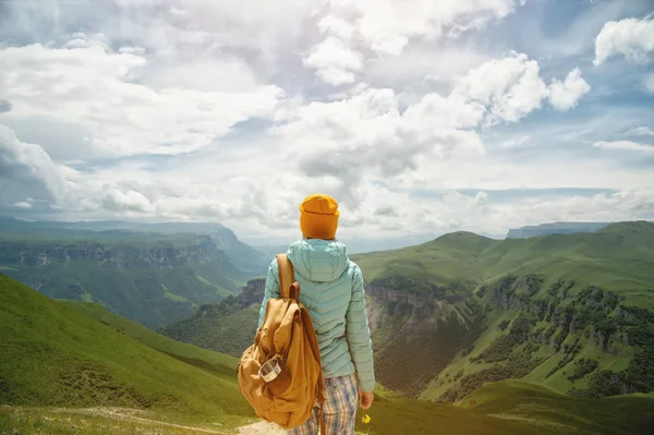 A kilátás a hátán egy turista lány egy hátizsák áll, és nézi a hegyi zöld völgyek és fennsík egy napsütéses napon az ég és a felhők. Utazási és idegenforgalmi koncepció — Stock Fotó