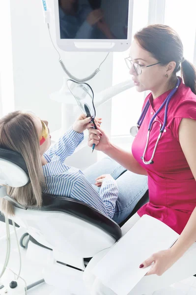 Γιατρό. Γυναίκα. Οδοντίατρος που μιλάει σε έναν νεαρό ασθενή που κάθεται στην καρέκλα οδοντιάτρου στο ιατρικό γραφείο. Δείχνει στον καθρέφτη το χαμόγελό της. — Φωτογραφία Αρχείου