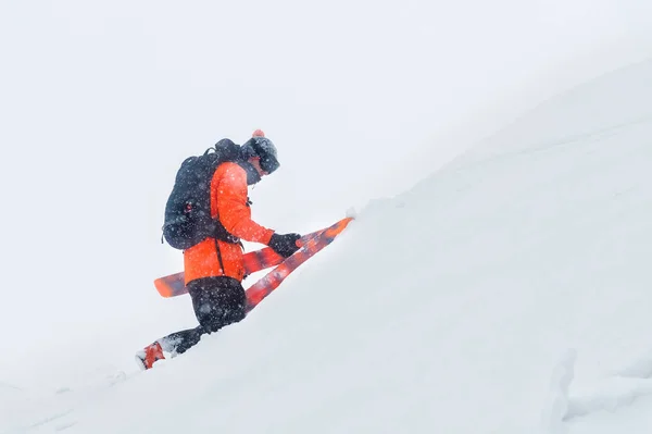 Porträt eines professionellen Skifahrers, der im Schneesturm einen Hang mit Skiern erklimmt. das Konzept des Reitens bei schlechtem Wetter — Stockfoto