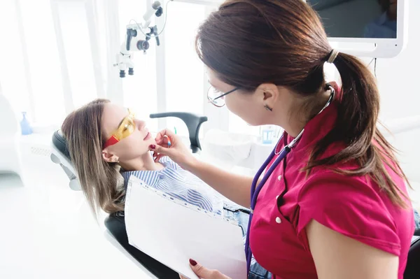 Οδοντίατρος γυναίκα γιατρός μιλάει με ένα νεαρό ασθενή κάθεται στην καρέκλα του οδοντιάτρου σε ένα ιατρικό γραφείο. Η πρώτη συζήτηση με τον πελάτη και την εξωτερική οπτική επιθεώρηση — Φωτογραφία Αρχείου