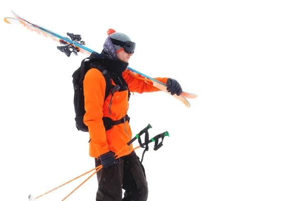 Portret van een professionele atleet skiër in een oranje jasje met een zwart masker en met ski's op zijn schouder kijkt in de camera. Geïsoleerd op wit — Stockfoto