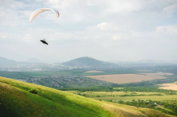 Un parapente vuela en el cielo en un traje de capullo en un parapente sobre el campo caucásico con colinas y montañas. Parapente Concepto Deportivo — Foto de Stock