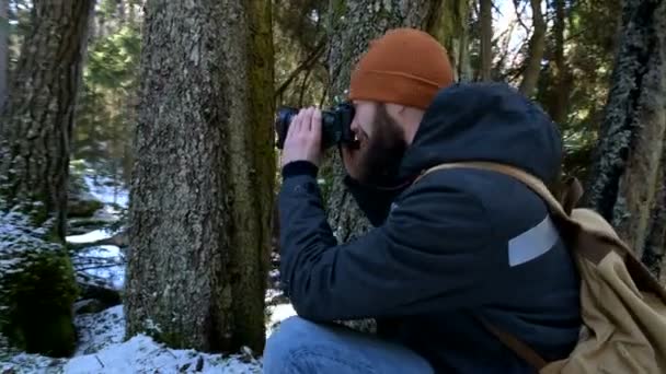 Vousatý mužský cestovatel s fotoaparátem v zimním lese si dělá fotky přírody. Cestovní koncept pro bloggery a fotoumělce — Stock video