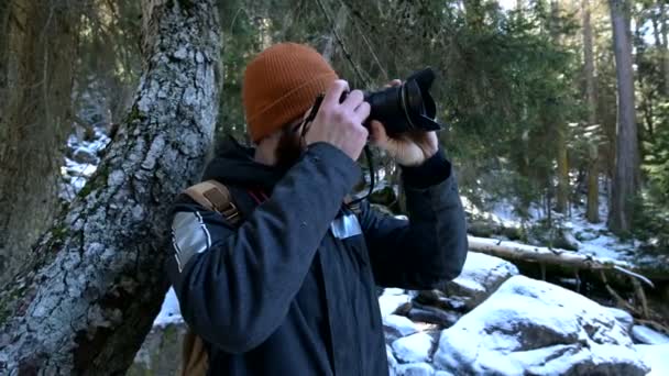 A bearded male traveler photographer with his camera in the winter forest takes pictures of nature. Travel concept for bloggers and photo artists — Stock Video