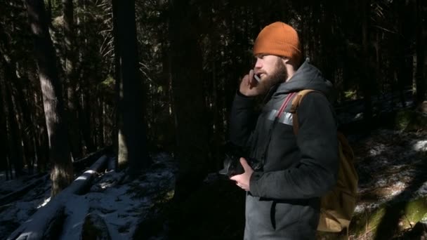 Бородач в шляпе разговаривает по мобильному телефону в хвойном лесу. Концепция сотовой связи в труднодоступных местах — стоковое видео