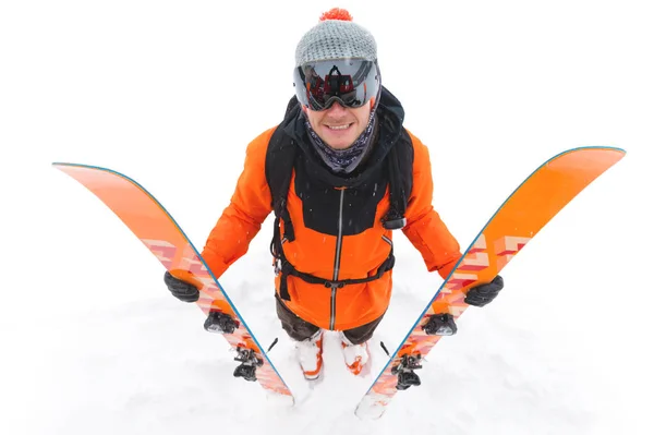 Een professionele skiër in een oranje zwart pak met een zwart ski-masker met ski's in zijn handen staat met een ontevreden massa tijdens een sneeuwstorm op een lichte achtergrond in de sneeuw — Stockfoto