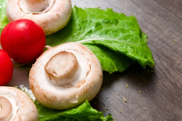 Primer plano de champiñones blancos con hojas de ensalada verde con tomate sobre una mesa de madera oscura. Comida vegetariana saludable — Foto de Stock