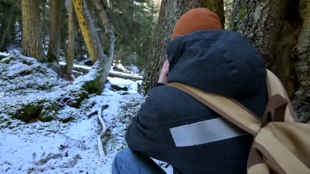 Een bebaarde mannelijke reiziger fotograaf met zijn camera in het winter bos neemt foto's van de natuur. Reis concept voor bloggers en foto artiesten — Stockvideo