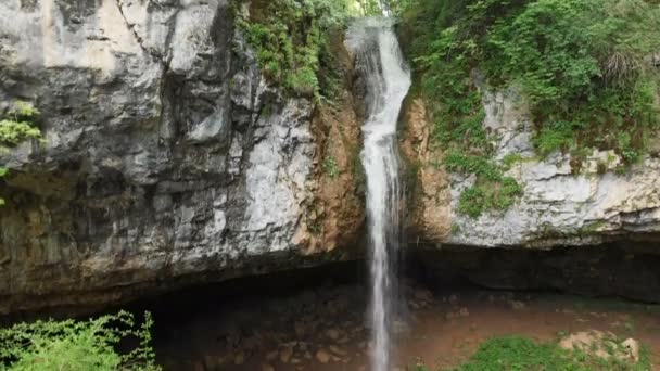 Vista aérea de un viajero masculino con una mochila de pie sobre las rocas frente a una majestuosa cascada y admirando la naturaleza en el bosque entre las rocas. Viajes video 4k — Vídeo de stock