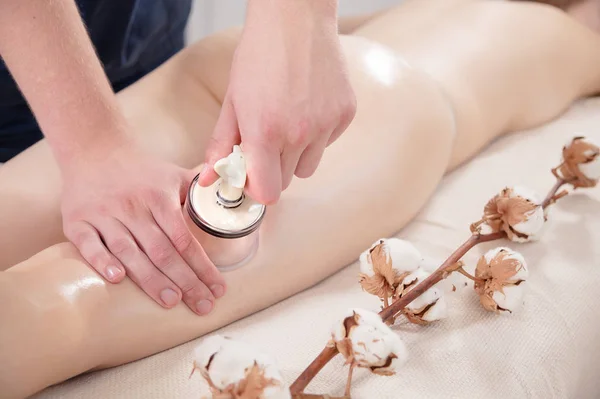 Close-up of a male physiotherapist massage therapist doing a vacuum can massage to a young girl on her hips next to cotton flowers. Tenderness and attention to health. Cellulite treatments.