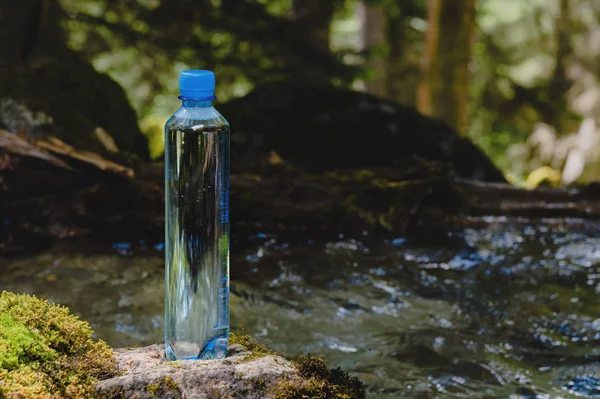 Plastikowa butelka niebieska Czapka ze świeżą wodą pitną na tle zielonego lasu stoi na kamieniu z mchem. Koncepcja czystej naturalnej wody górskiej — Zdjęcie stockowe