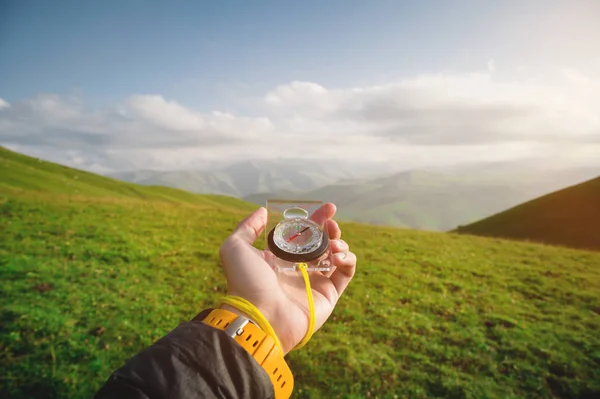 Mano masculina con una brújula magnética en el fondo de un hermoso paisaje al atardecer. El concepto de navegar la búsqueda de su propio camino y la orientación a los puntos cardinales — Foto de Stock