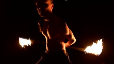 Close. Düşük anahtar. Uzun saçlı ve çıplak gövde ile genç erkek siyah bir gece video yavaş hareket açık havada yanan meşale döner. Modern fakir bir yanan personel ile hileler yapar