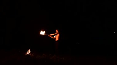 Düşük anahtar. Uzun saçlı ve çıplak gövde ile genç erkek siyah bir gece video yavaş hareket açık havada yanan meşale döner. Modern fakir bir yanan personel ile hileler yapar