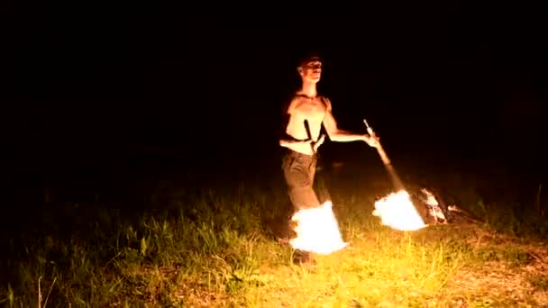 Low Key. Jonge man met lang haar en kale torso roteert brandende toorts buitenshuis op een zwarte nacht video Slow Motion. Moderne Fakir doet trucs met een brandend personeel — Stockvideo