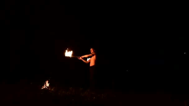 Low key. Young male with long hair and bare torso rotates burning torch outdoors on a black night video slow motion. Modern fakir does tricks with a burning staff — Stock Video