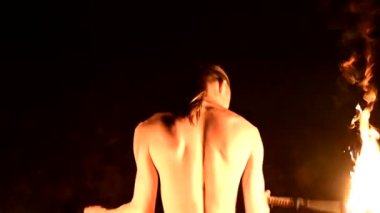 Yakın çekim arka görünüm. Düşük anahtar. Uzun saçlı ve çıplak gövdeli genç erkek siyah bir gece video yavaş hareket açık havada yanan meşale döner. Modern fakir yanan bir personel ile hileler yapar