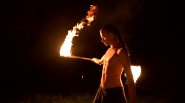 Düşük anahtar. Uzun saçlı ve çıplak gövde ile genç erkek siyah bir gece video yavaş hareket açık havada yanan meşale döner. Modern fakir bir yanan personel ile hileler yapar