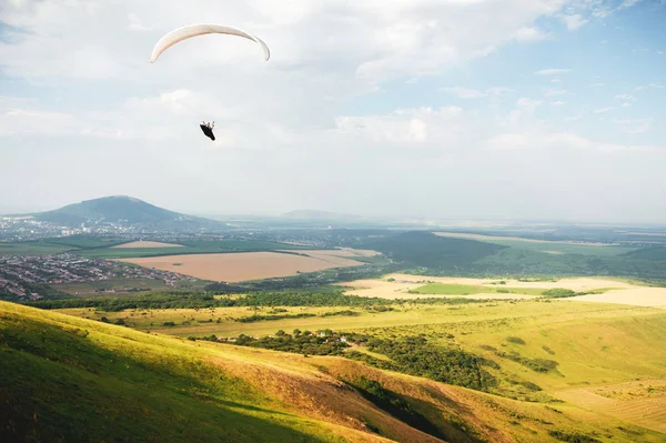 Un parapente vuela en el cielo en un traje de capullo en un parapente sobre el campo caucásico con colinas y montañas. Parapente Concepto Deportivo — Foto de Stock