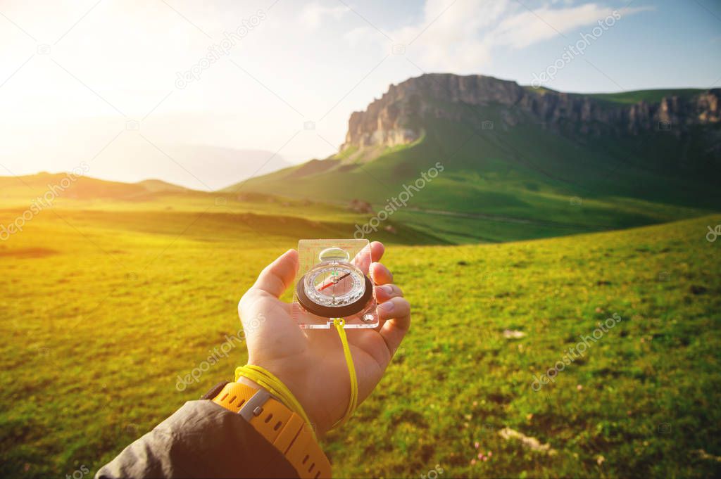 Male hand with a magnetic compass ea against the backdrop of a beautiful landscape at sunset. The concept of navigating the search for your own path and orientation to the cardinal points