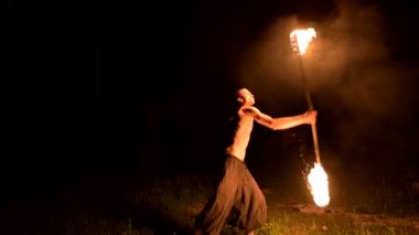 Düşük anahtar. Uzun saçlı ve çıplak gövde ile genç erkek siyah bir gece video yavaş hareket açık havada yanan meşale döner. Modern fakir bir yanan personel ile hileler yapar