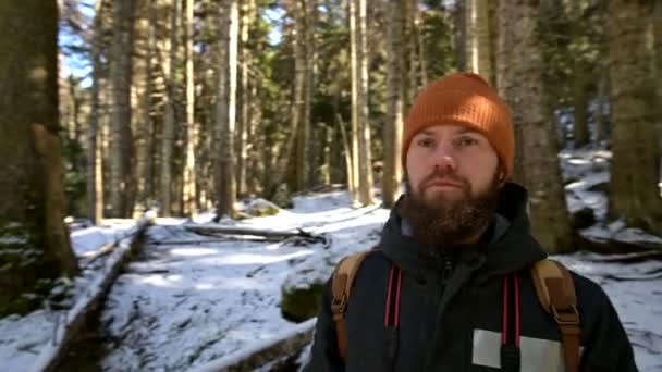 Retrato de un joven barbudo con una mochila en un bosque invernal de coníferas — Vídeo de stock