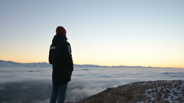 Вид ззаду. Самотній чоловік високо в горах дивиться на розташування сонця і горизонту заходу сонця з долиною, наповненою хмарами. Поняття туризму подорожей і чоловічої самотності — стокове відео