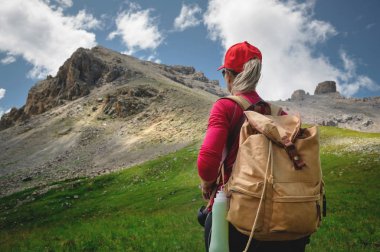 Kırmızı şapkalı güneş gözlüğü ve sarı sırt çantası ile arka Kız atlet görünümü Kafkasya'nın epik kayalıkların arka plan karşı yeşil bir yamaç üzerinde duruyor