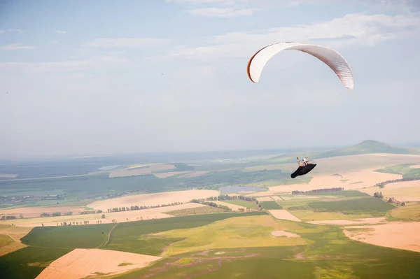 Ein Gleitschirmflieger fliegt im Kokon-Anzug auf einem Gleitschirm über die kaukasische Landschaft mit Hügeln und Bergen. Gleitschirmsportkonzept — Stockfoto