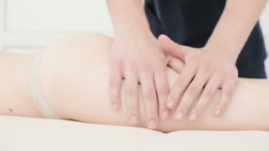 Yakın çekim bir erkek fizyoterapist pamuk bir delikanlı yanında profesyonel bir spa salonunda genç bir kadının kalça ve kalça ısınmak için hafif bir masaj yapıyor. 4k masaj vücut bakım konsepti