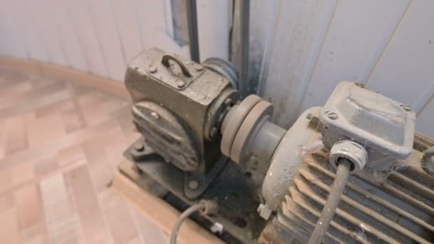 Un vieux moteur électrique recouvert de poussière et de saleté tourne une poulie à deux fils à travers une boîte de vitesses cardan avec un entraînement par courroie vers un autre mécanisme. Le concept des vieux moteurs et équipements électriques 