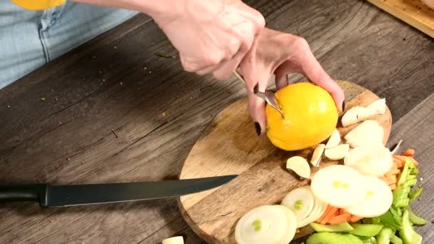 Крупный план женских рук, делающих отверстия в лимоне для сжатия на разделочной доске рядом с рублеными листьями мяты и огурцами. Здоровое и здоровое вегетарианское питание — стоковое видео