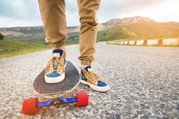 Nahaufnahme von Männerbeinen in Lumpensneakers auf einem Longboard vor dem Hintergrund des Asphalts bei Sonnenuntergang. großes Skateboard mit Mannsbeinen. Jugendfreizeitkonzept — Stockfoto