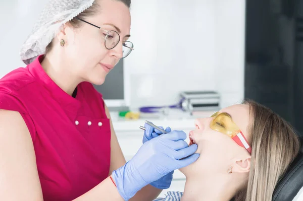 Στο οδοντιατρείο. Μια γυναίκα οδοντίατρος με γυαλιά ετοιμάζεται να κάνει ένα καστ από το σαγόνι ενός νεαρού κοριτσιού ασθενή. Φροντίδα καθαρό στόμα — Φωτογραφία Αρχείου