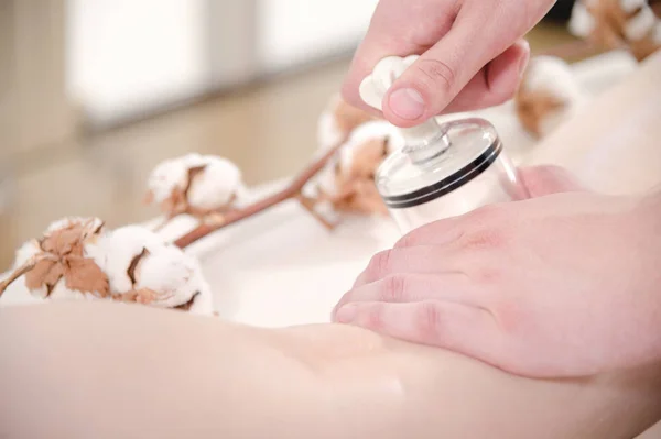 Close-up of a male physiotherapist massage therapist doing a vacuum can massage to a young girl on her hips next to cotton flowers. Tenderness and attention to health. Cellulite treatments. — Stock Photo, Image