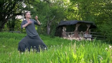 Genel plan Hint giysi ve pantolon Aladdin uygulamaları qigong genç bir adam eski bir kulübe 4k yanında yaz açık havada qi enerji ile çalışan egzersizleri yaparken