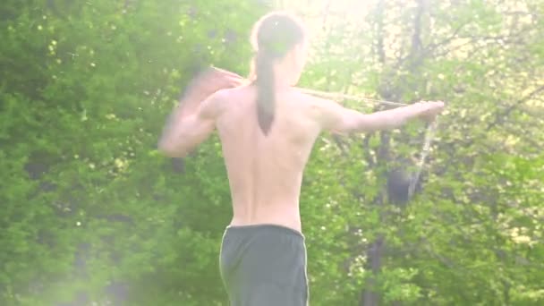 Tiro médio Um jovem com cabelos longos e um tronco nu é treinado em arte marcial e antes de falar com uma equipe ou carregar corda em rotação ao ar livre em uma manhã de verão. ângulo baixo — Vídeo de Stock